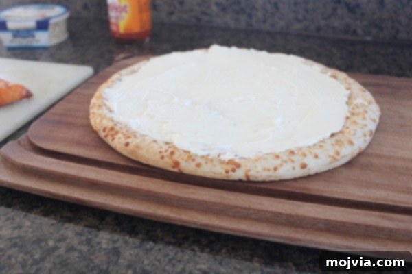 Loaded Buffalo Chicken Pizza 4 A pre-cooked pizza crust covered with a smooth, creamy cheese sauce, forming the base for the buffalo chicken dip pizza.