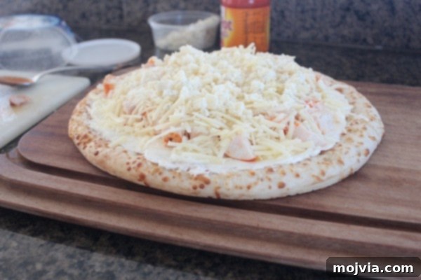 Loaded Buffalo Chicken Pizza 6 An uncooked Buffalo Chicken Dip Pizza fully loaded with various cheeses on top of the chicken and sauce layers, resting on a wooden cutting board.