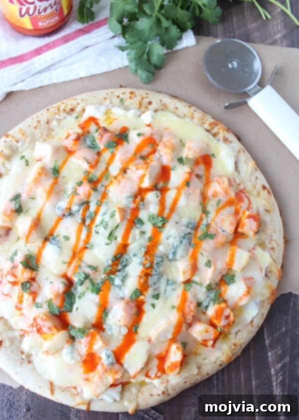Loaded Buffalo Chicken Pizza 9 A whole Buffalo Chicken Dip Pizza sitting on a wooden surface next to a pizza cutter, ready to be sliced.