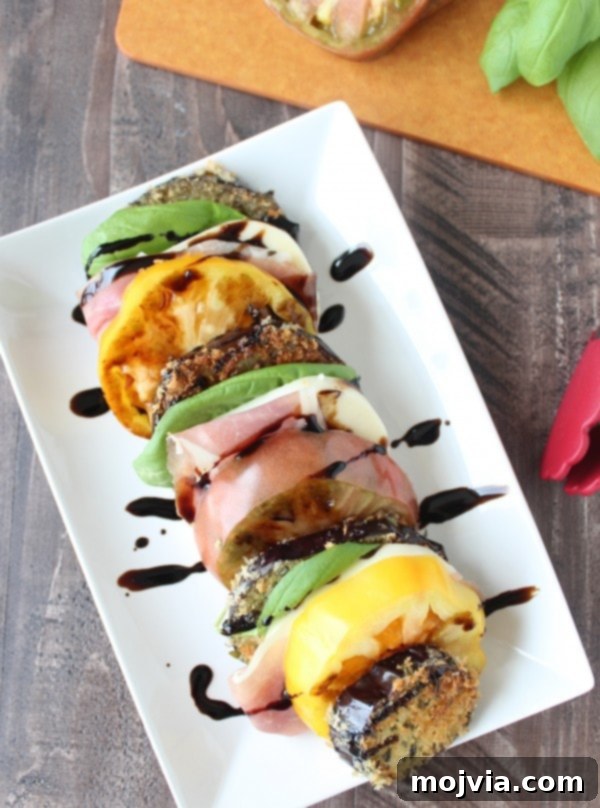 Elevated Caprese with Crispy Eggplant and Prosciutto 8 Eggplant, Prosciutto, fresh basil, mozzarella, and tomatoes on a white plate drizzled with a balsamic glaze.