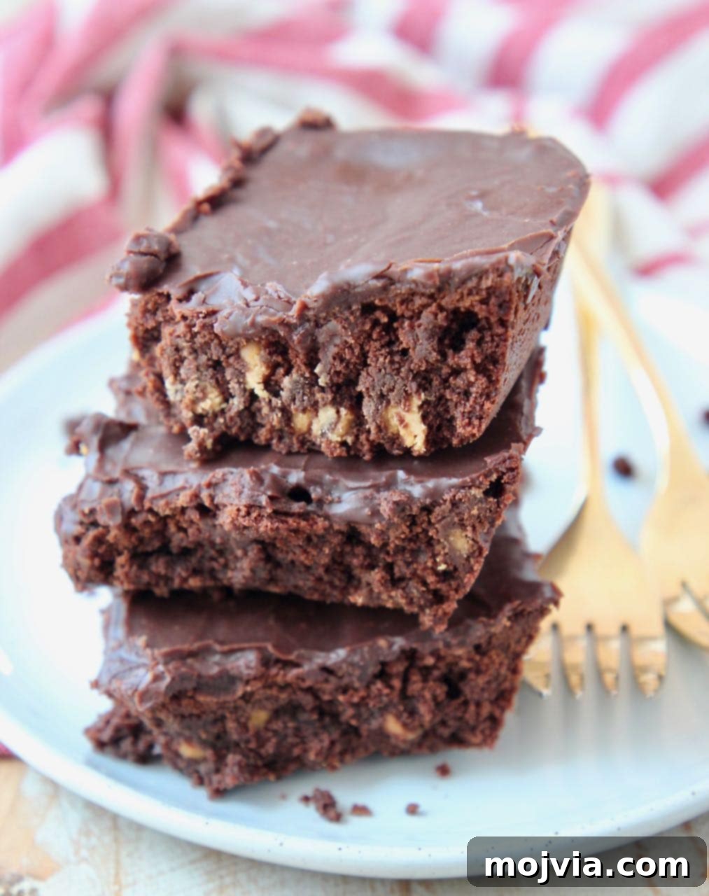 Three stacked brownies on a white plate with gold forks on the side