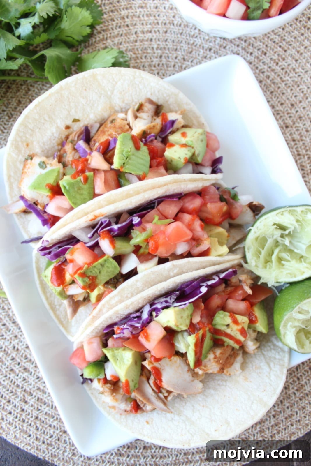fish tacos on white plate, topped with diced avocado and hot sauce