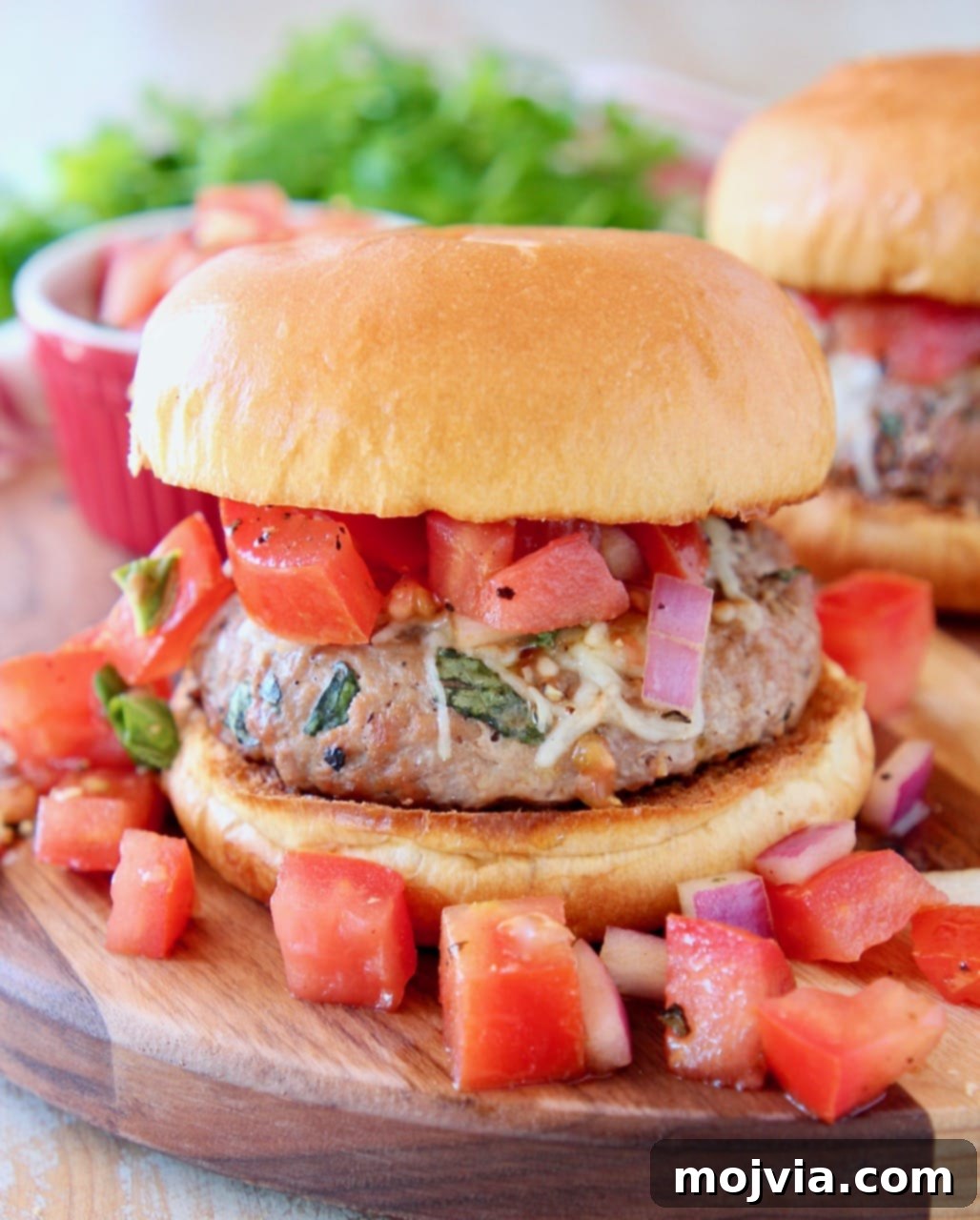 Turkey burger on bun on wood cutting board topped with diced tomato bruschetta