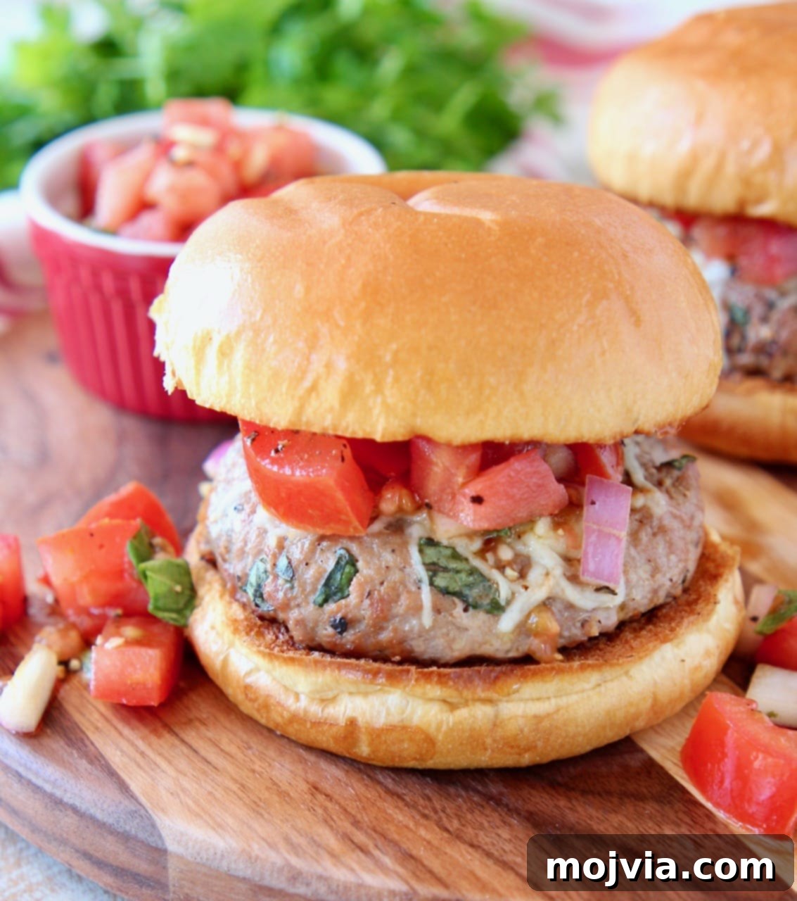Turkey burger on bun topped with diced tomatoes and onions on wood cutting board