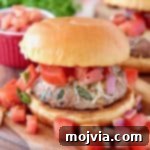 Turkey burger on bun on wood cutting board topped with diced tomatoes