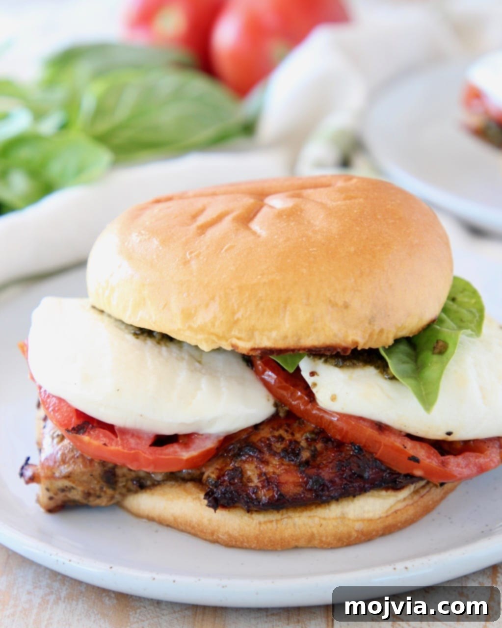 Grilled chicken sandwich with tomatoes and mozzarella cheese on white plate, garnished with basil