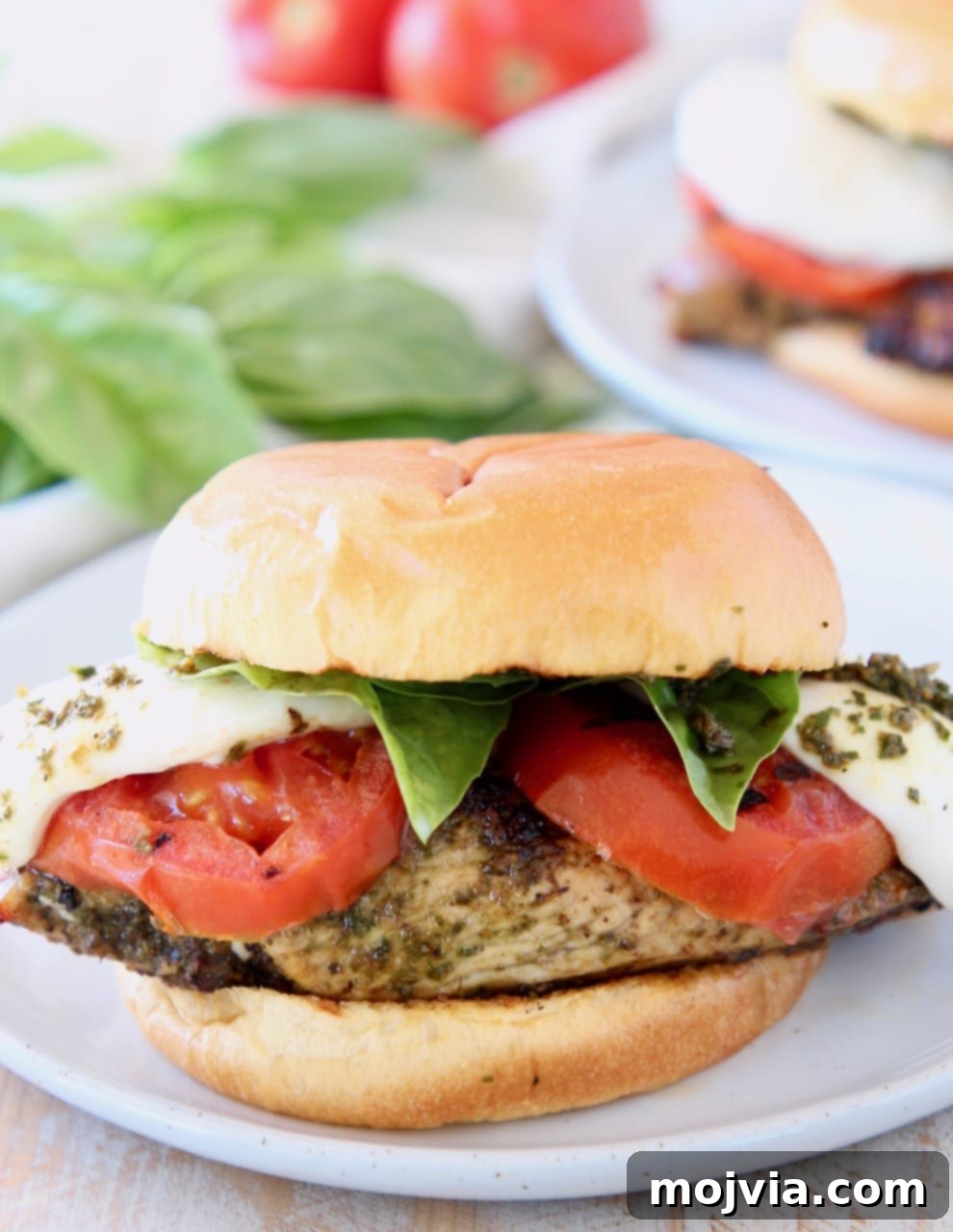 Pesto grilled chicken sandwich with grilled tomatoes and mozzarella cheese on a wooden board