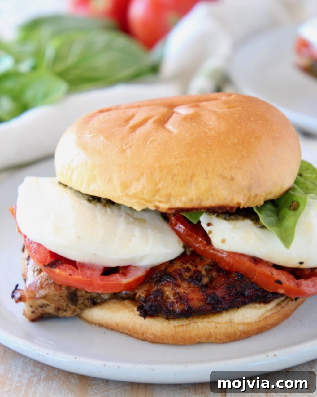 Grilled chicken sandwich with tomatoes, basil and mozzarella cheese on white plate with a fork