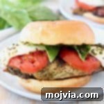 Caprese grilled chicken sandwich on white plate with fresh basil in background