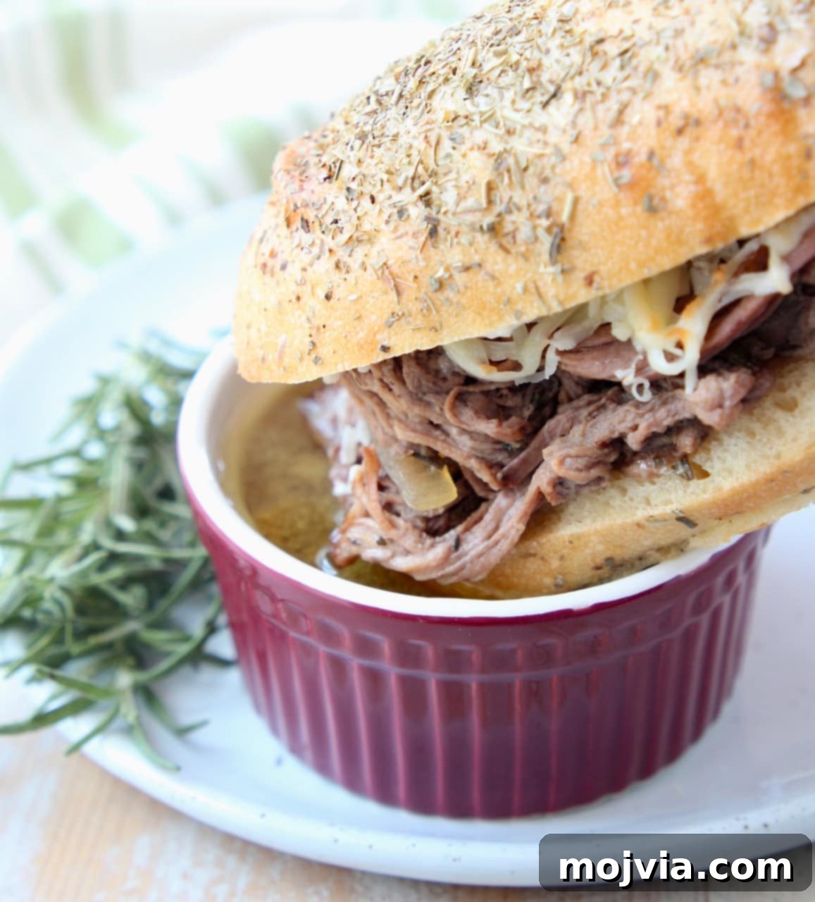 Tri Tip French Dip Sandwich being dipped into a bowl of au jus