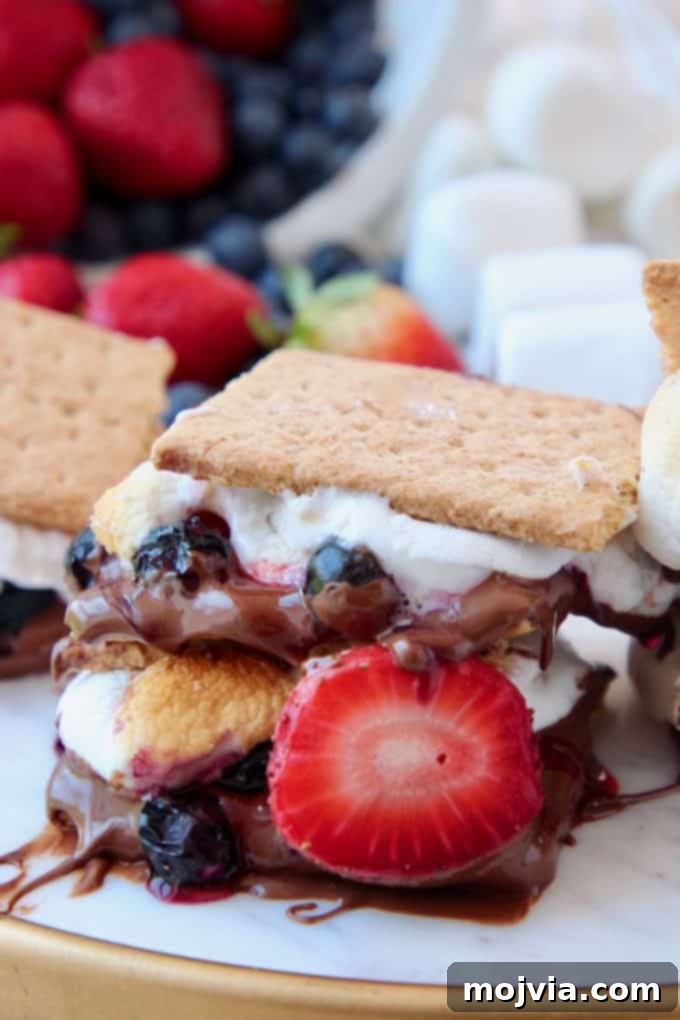 Smores with strawberries and blueberries stacked up on serving platter, showcasing the melted chocolate and toasted marshmallows