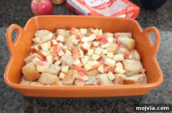 unbaked bread pudding in orange baking dish with diced apples on top