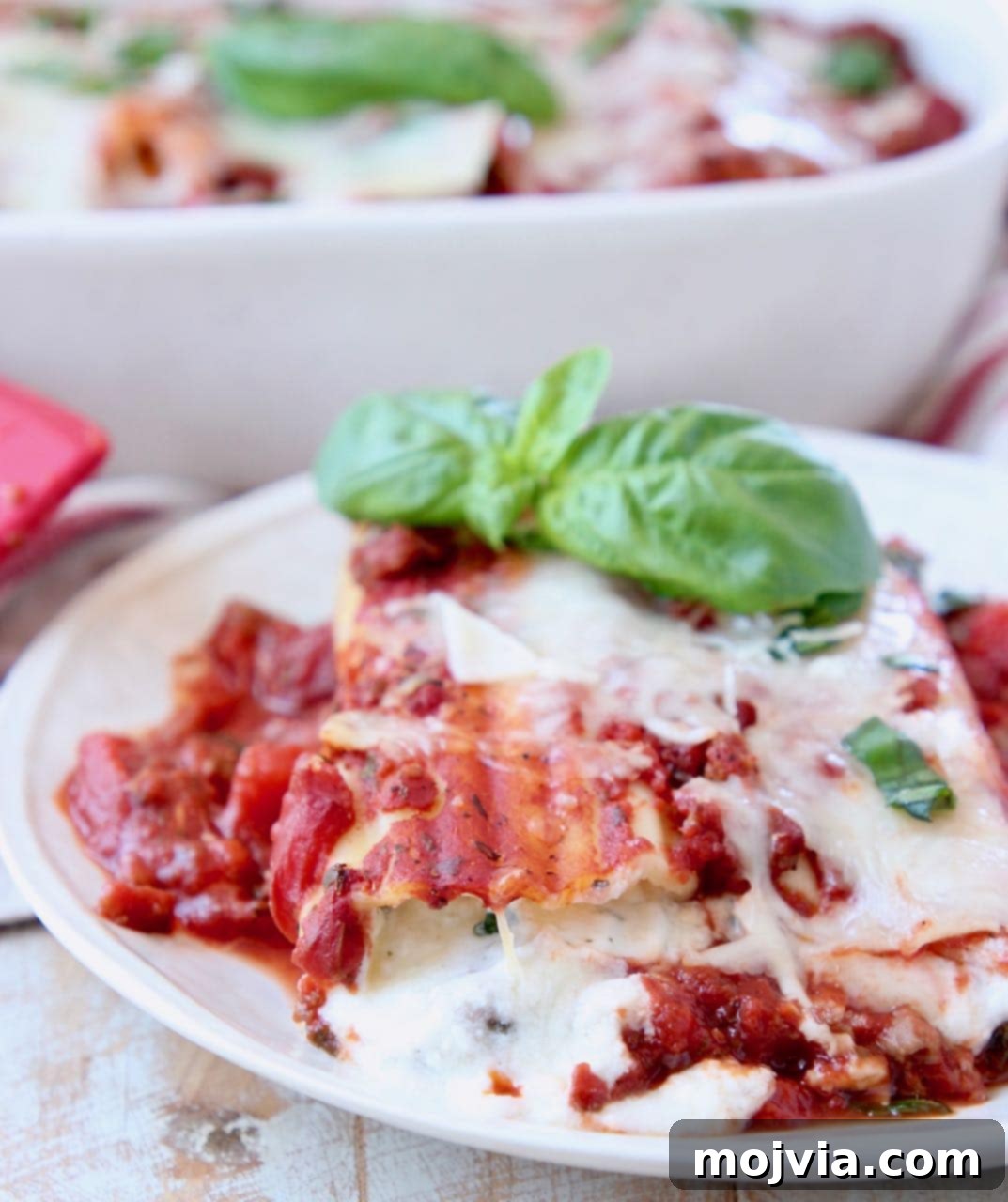 Hearty Three-Cheese Manicotti with Robust Italian Sausage Marinara 3 Close-up of cheese manicotti on a white plate, garnished with marinara sauce and fresh basil leaves.