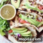 Three ground beef tacos on wood tray with avocado and salsa
