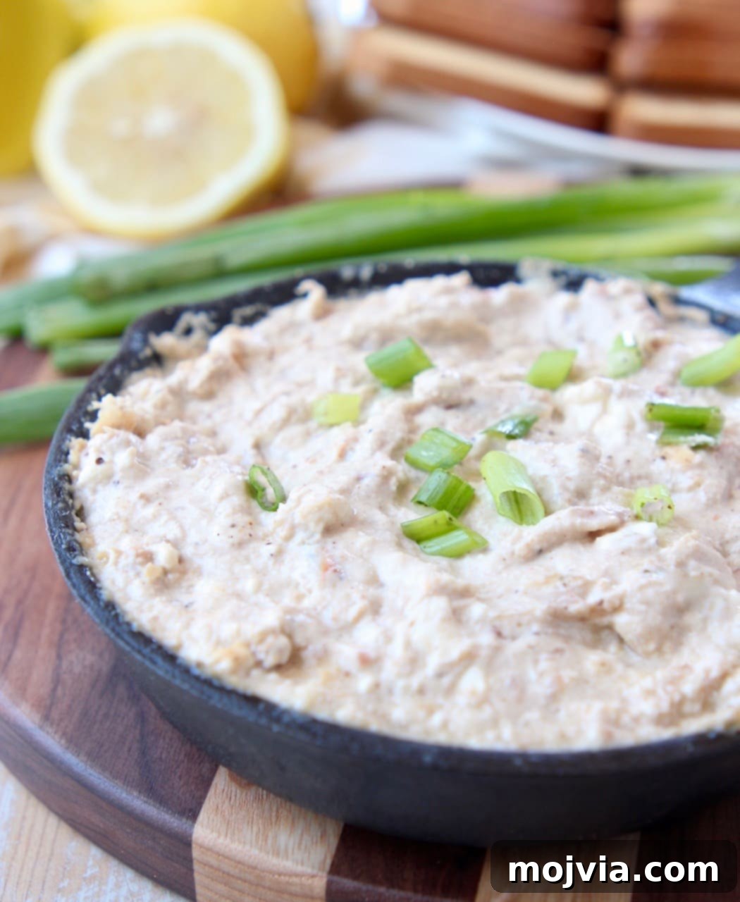 Baked Crab Dip 2 Hot crab dip in cast iron skillet, sitting on wood cutting board, garnished with fresh herbs
