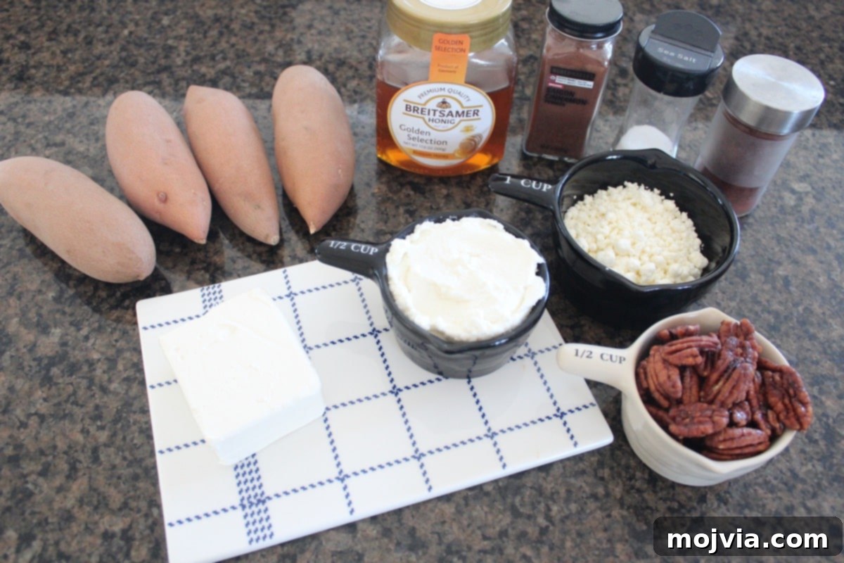 Raw ingredients for Baked Sweet Potato and Three Cheese Dip laid out on a granite countertop: sweet potatoes, cream cheese, ricotta, goat cheese, honey, chipotle powder, cinnamon, salt, pecans, maple syrup.