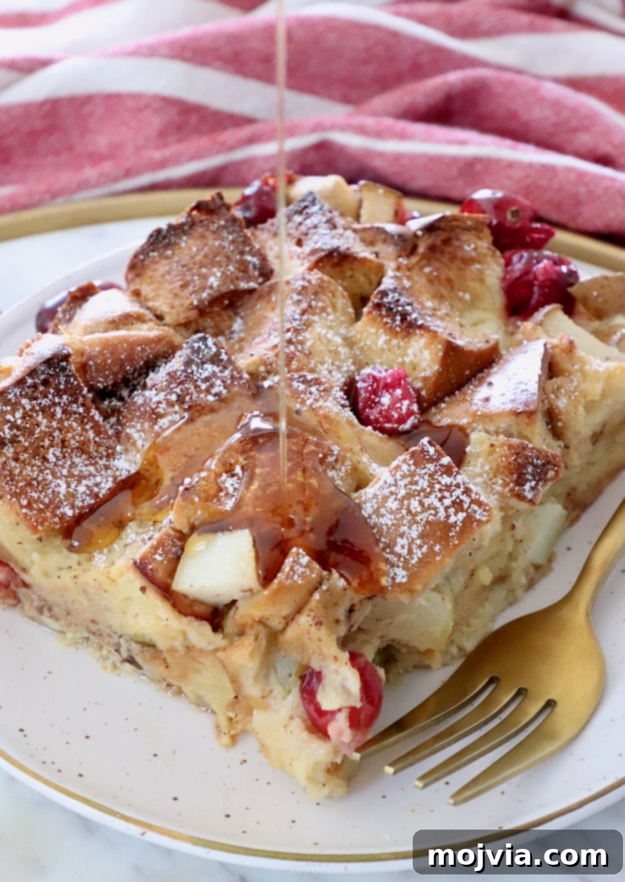 Syrup being poured over a slice of cranberry pear French toast casserole on a white plate with a fork, ready to be enjoyed.