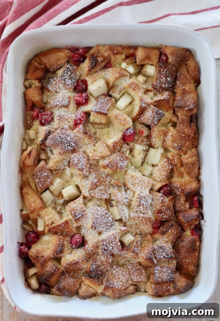 A baked cranberry pear French toast casserole in a ceramic dish, golden brown and ready to be served, showcasing its delicious crust.
