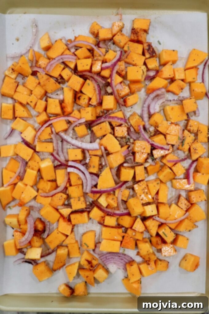 Golden Roasted Butternut Salad 4 cubed butternut squash with sliced onions and minced garlic on a parchment paper lined baking sheet