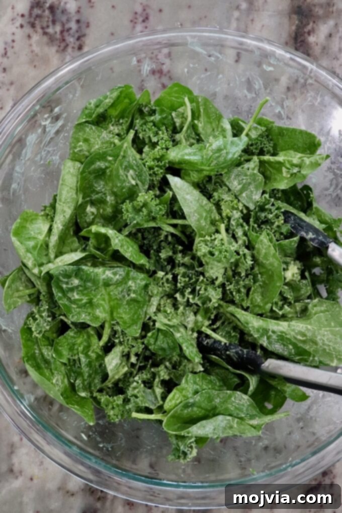 Golden Roasted Butternut Salad 7 baby spinach and kale tossed in a creamy dressing in a large glass bowl with tongs