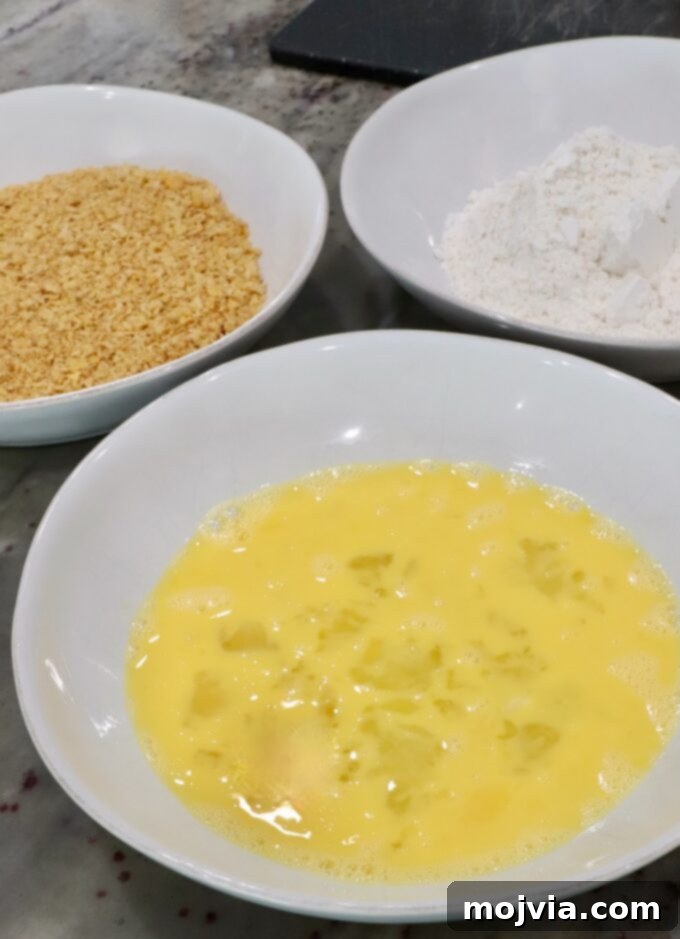 Sweet Heat Chipotle Chicken Tenders 5 Three shallow bowls on a countertop for the breading station: eggs, flour, and cornflakes.