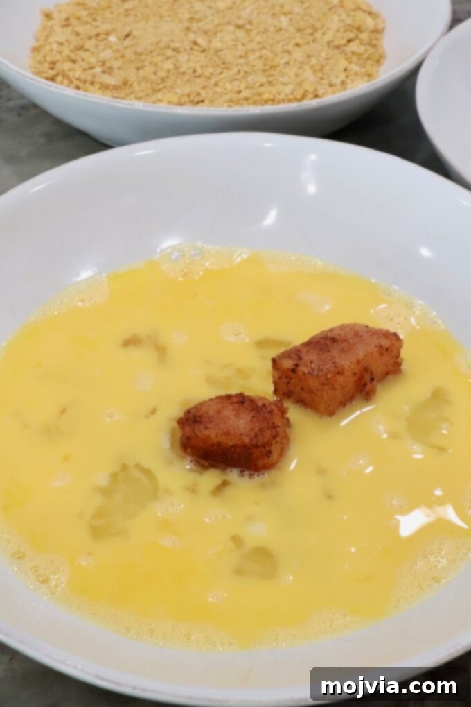 Sweet Heat Chipotle Chicken Tenders 8 Seasoned raw chicken pieces being dipped into a bowl of whisked eggs.