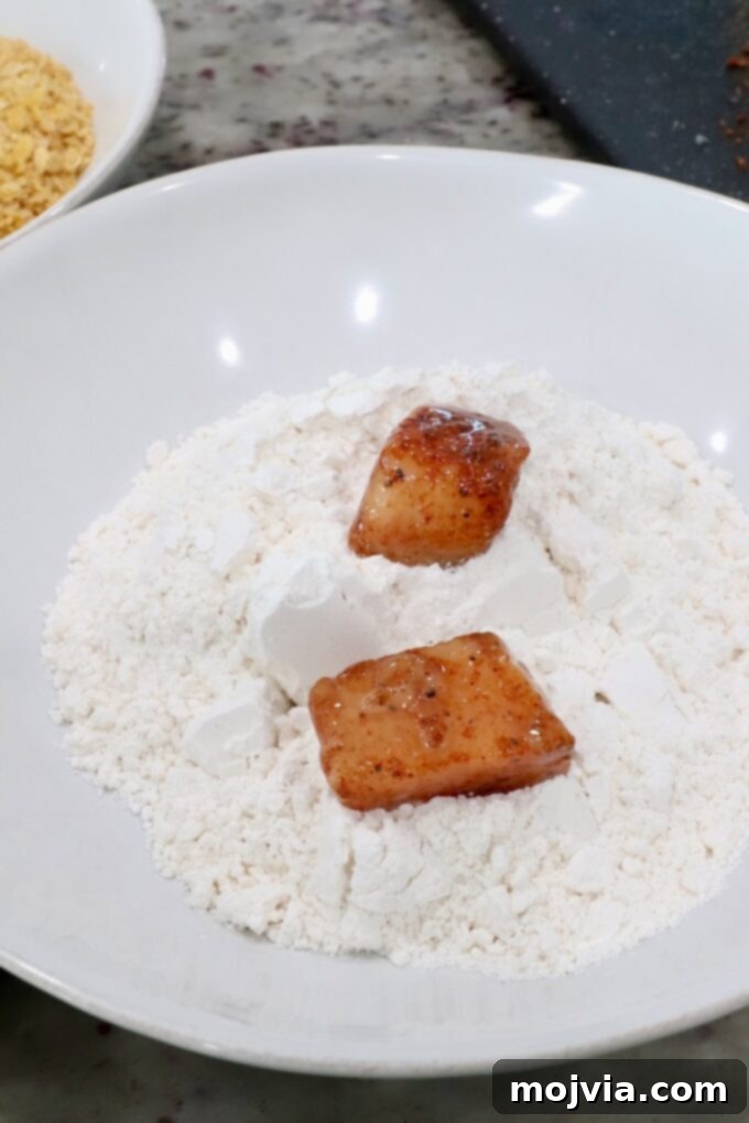 Sweet Heat Chipotle Chicken Tenders 9 Seasoned, egg-dipped raw chicken pieces being coated in a bowl of flour.