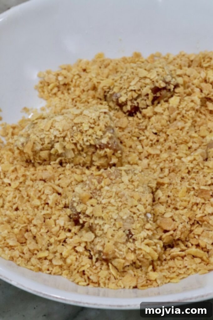 Sweet Heat Chipotle Chicken Tenders 10 Flour-coated chicken pieces being pressed into a bowl of crushed corn flakes.