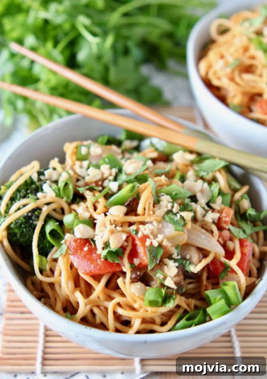 Creamy Thai Peanut Noodles with Fresh Vegetables 3 A close-up of ramen noodles and colorful vegetables perfectly coated in Thai peanut sauce, presented in a bowl with chopsticks resting beside it.