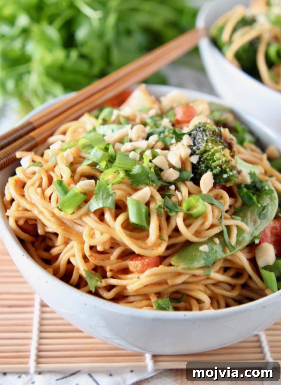 Creamy Thai Peanut Noodles with Fresh Vegetables 4 A beautifully presented bowl of Thai Peanut Noodles, garnished with a generous sprinkle of chopped peanuts and vibrant green onions. Chopsticks are placed artistically on the side, inviting you to dig in.