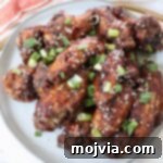 cooked chicken wings tossed in sauce and piled up on a plate with diced green onions and sesame seeds