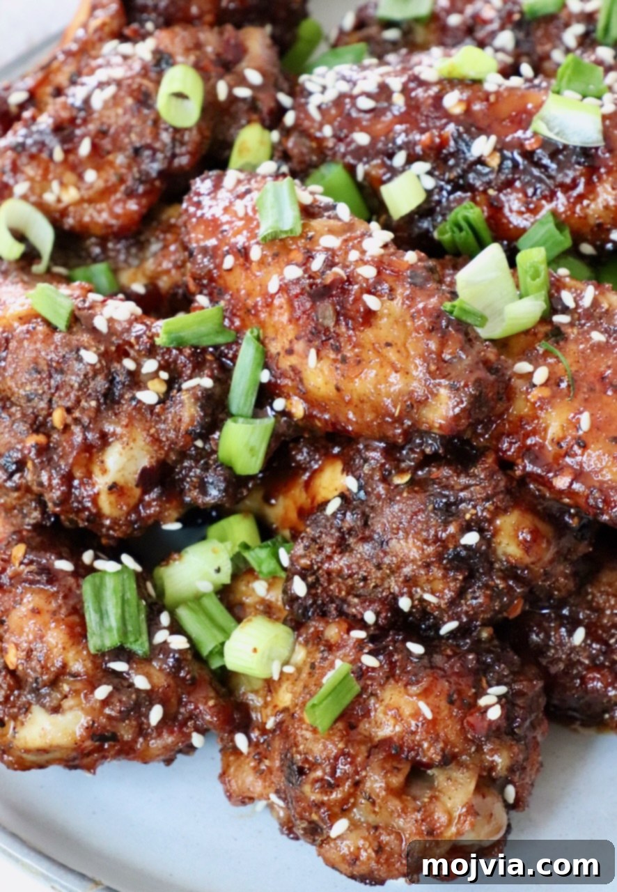 cooked chicken wings tossed in sauce piled up on a plate, topped with diced green onions and sesame seeds