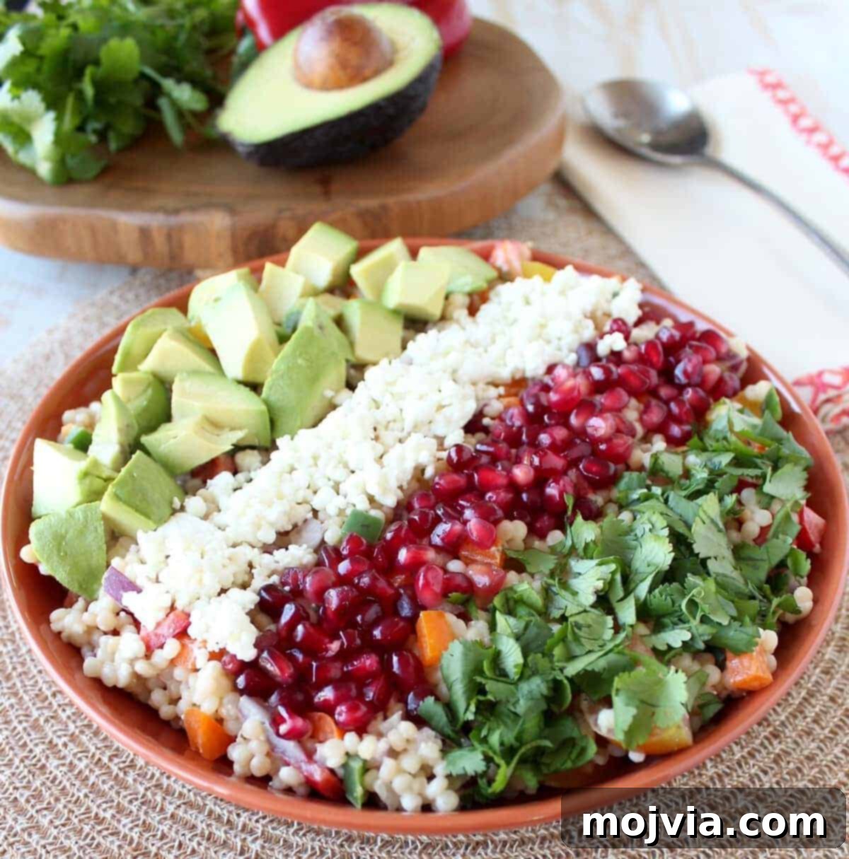 Creamy Avocado Pearl Couscous Salad 2 Vibrant Israeli couscous salad in an orange bowl, garnished with pomegranate seeds, cilantro, goat cheese, and avocado