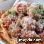 Set-and-Forget Slow Cooker Meatballs and Marinara 14 cooked meatballs on top of spaghetti and tomato sauce in bowl with fork