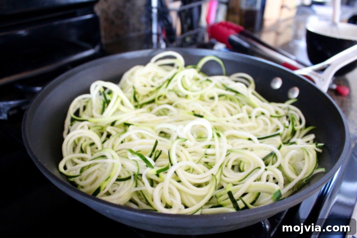 Fresh zucchini noodles cooking in a large skillet with garlic over medium-high heat