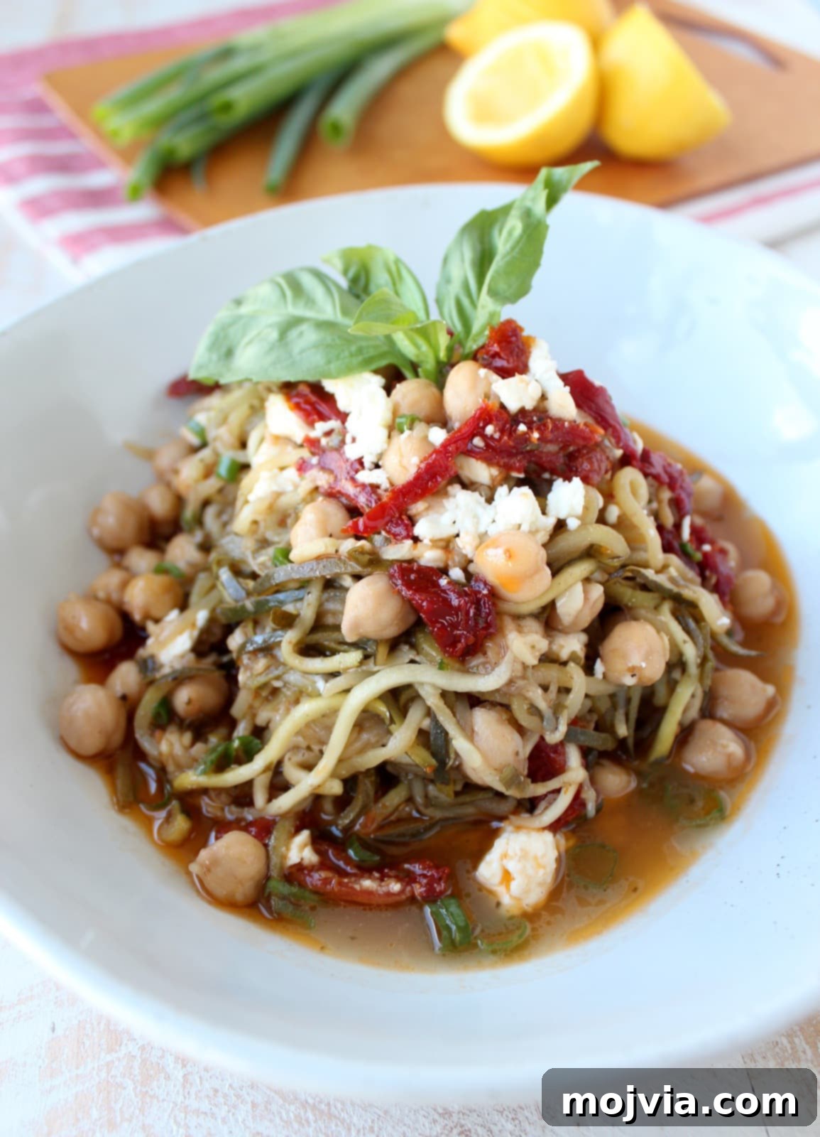 Finished Greek Zucchini Noodles in a bowl, topped with feta cheese and sun-dried tomatoes, ready for serving