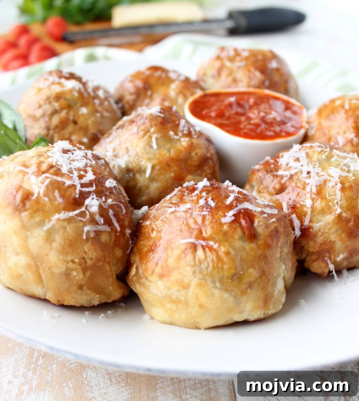 Golden Pastry Meatballs with a Melted Mozzarella Core 2 Golden-baked puff pastry wrapped meatballs on a pristine white plate, garnished with freshly shredded Parmesan cheese, ready to be served.
