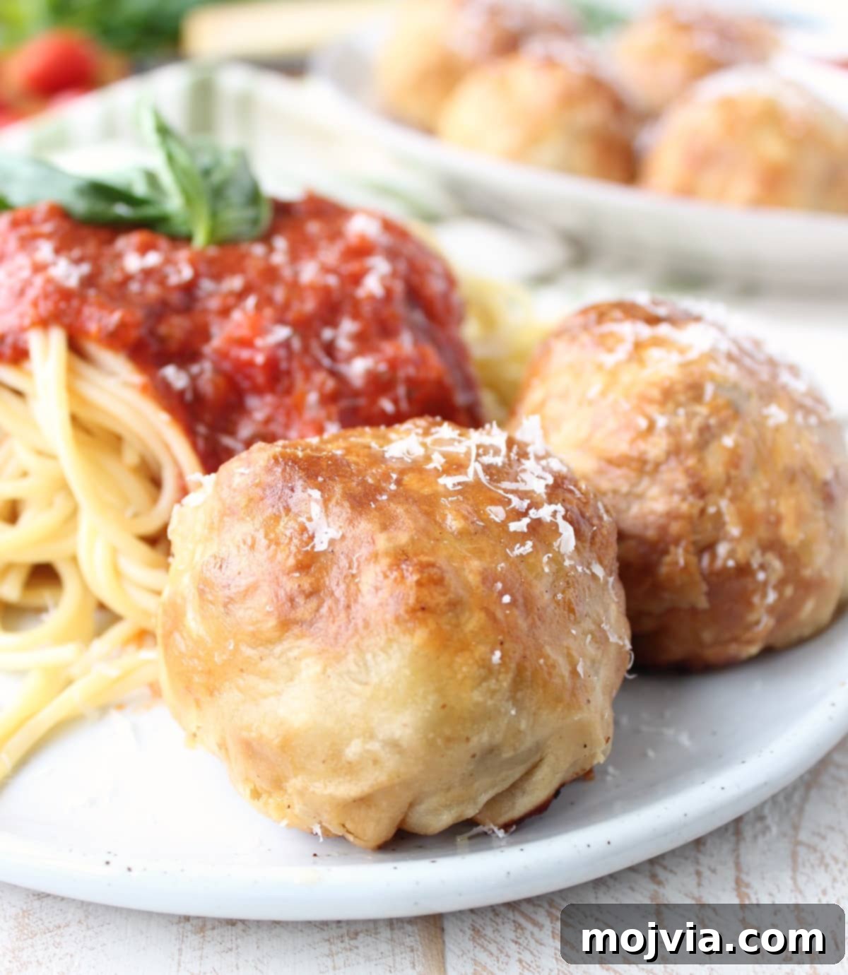 Golden Pastry Meatballs with a Melted Mozzarella Core 4 Puff Pastry Wrapped Meatballs beautifully arranged on a plate with fresh spaghetti and a rich marinara sauce, garnished with herbs.