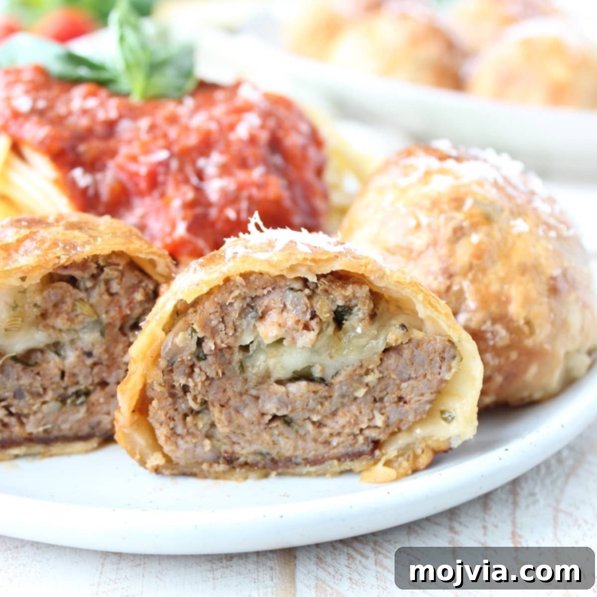 Golden Pastry Meatballs with a Melted Mozzarella Core 5 A single Mozzarella Stuffed Meatball Wellington, meticulously cut in half to showcase its flaky pastry and the luscious, melted cheese within, presented on a simple plate.