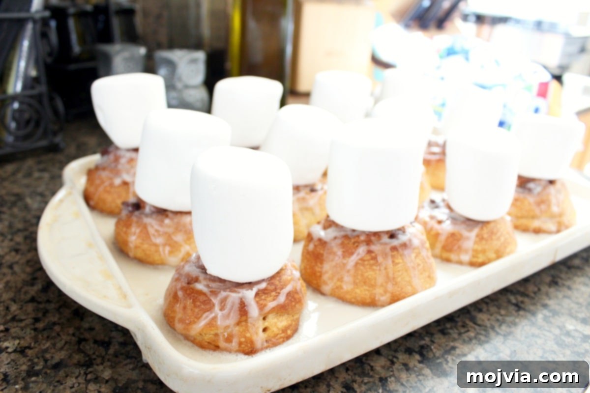 Large marshmallows placed on top of iced S'Mores Cinnamon Rolls, ready for broiling.