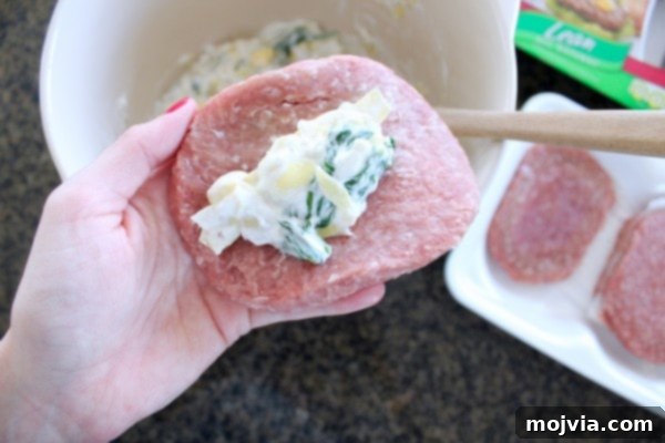 Gourmet Spinach Artichoke Turkey Burgers 6 A turkey burger patty being stuffed with spinach artichoke dip by hand