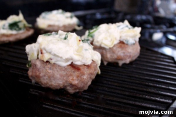 Gourmet Spinach Artichoke Turkey Burgers 7 Stuffed turkey burgers cooking on a grill pan, topped with additional spinach artichoke dip