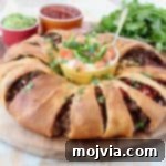 A beautifully baked taco ring with crescent rolls on a wooden cutting board, surrounded by small ramekins of sour cream, salsa, and guacamole for dipping.