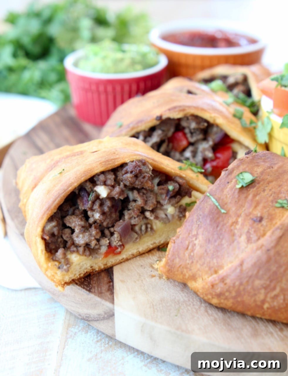 Fiesta Taco Ring 5 A freshly baked crescent roll taco ring, sliced to reveal the savory ground beef, onion, and bell pepper filling, resting on a rustic wooden cutting board.