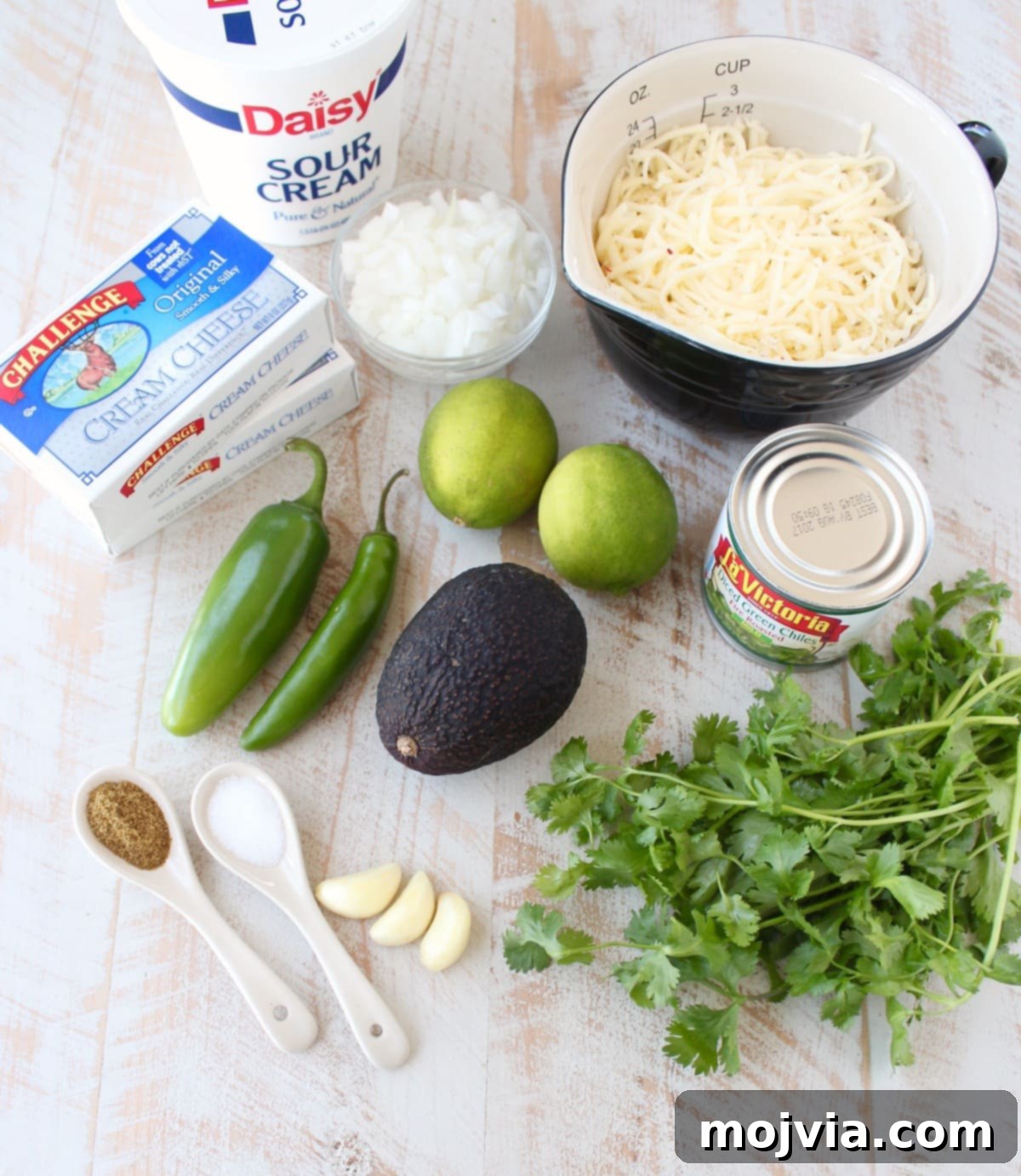 Set It and Forget It Green Chile Queso Blanco 3 Fresh ingredients for queso blanco dip laid out on a white wooden board, including onions, peppers, avocado, lime, and cilantro.