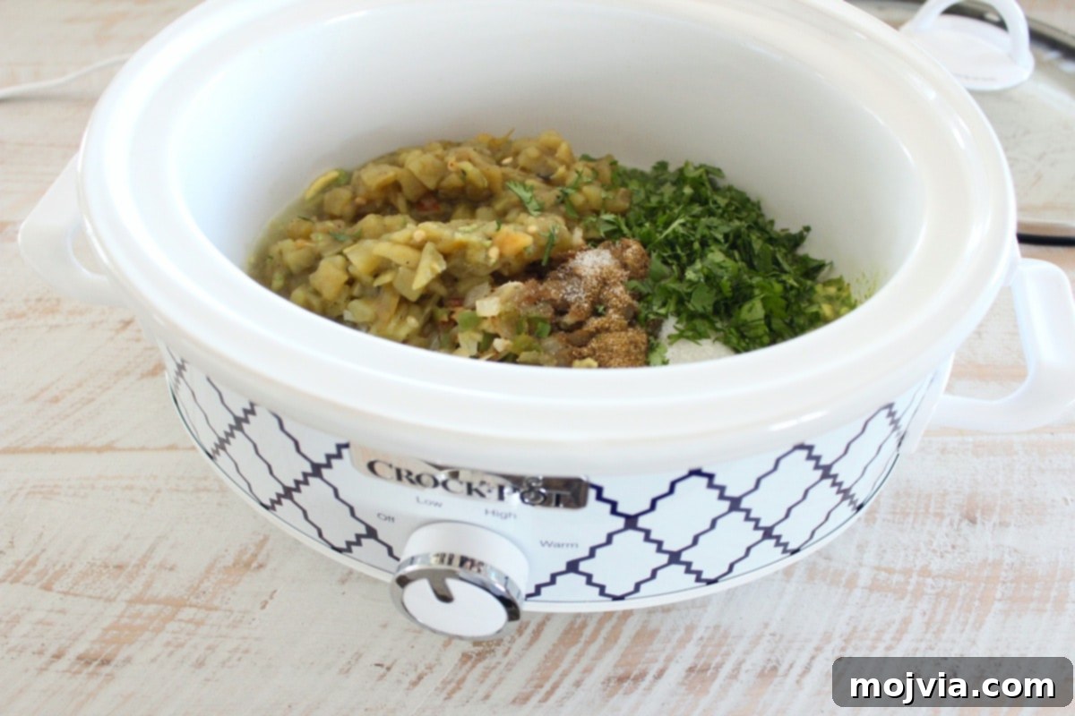 Set It and Forget It Green Chile Queso Blanco 4 Diced green chilies, cilantro, and various spices arranged in a slow cooker, ready for mixing.
