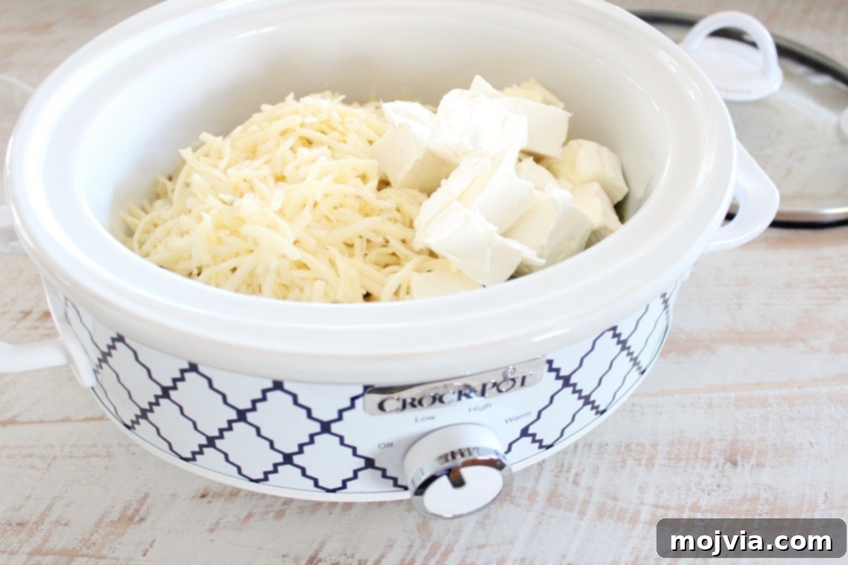 Set It and Forget It Green Chile Queso Blanco 5 Cubed cream cheese and shredded pepper jack cheese added to the slow cooker, ready to melt into a creamy dip.