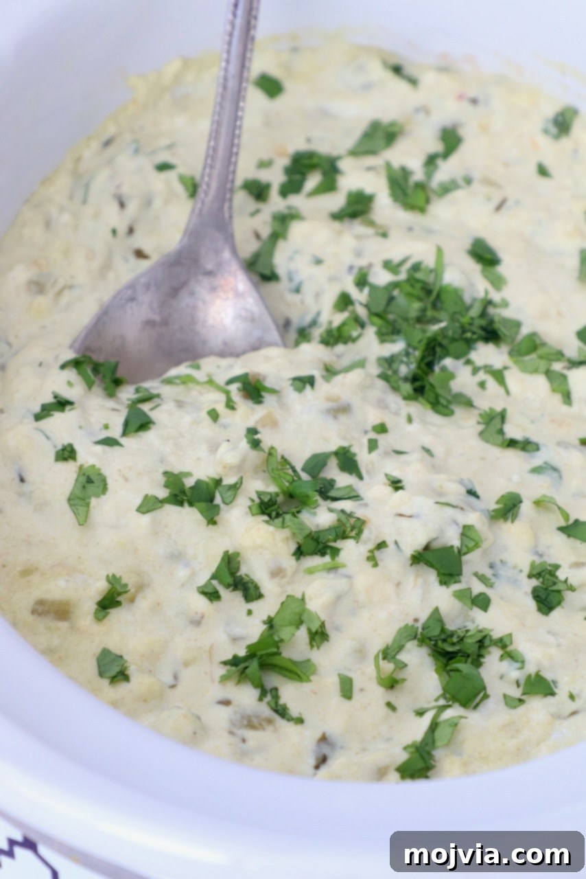 Set It and Forget It Green Chile Queso Blanco 7 Close-up of creamy white queso in a slow cooker with a serving spoon, ready to be dished out.