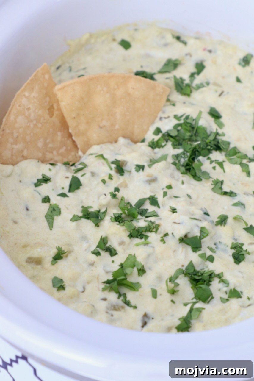 Set It and Forget It Green Chile Queso Blanco 8 White queso dip in a slow cooker, garnished with fresh cilantro, with tortilla chips dipped in.