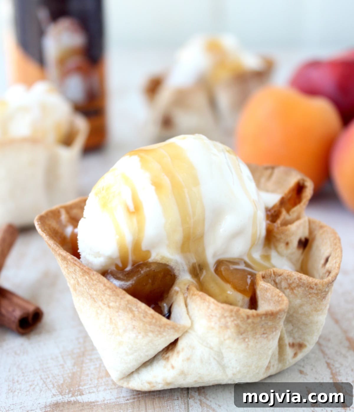 Effortless Fruit-Filled Dessert Shells 8 crispy taco shell cups filled with cooked fruit, topped with a scoop of ice cream and caramel syrup on a white wood board